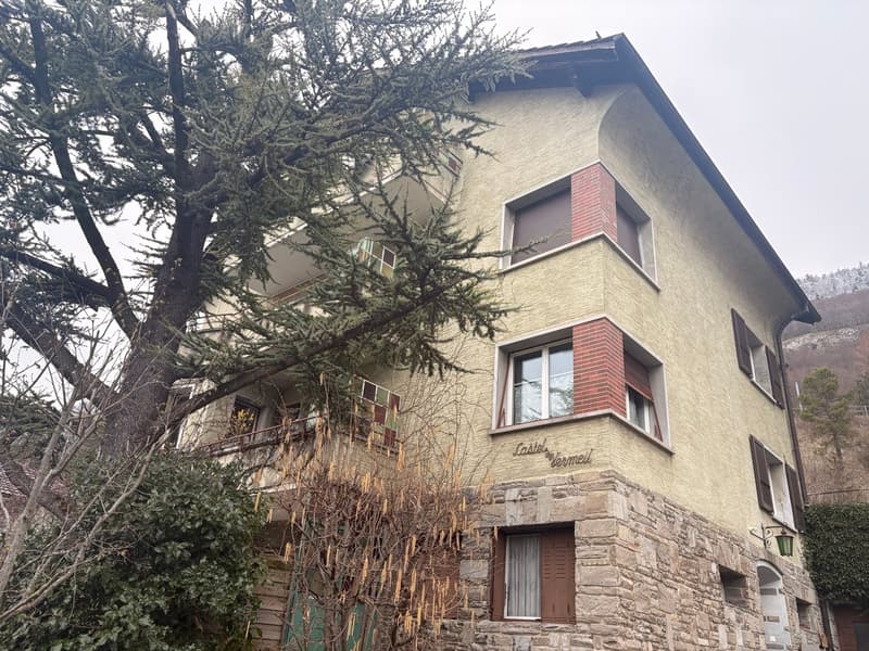 3 story house, beige stucco with red brick accents, multiple balconies, tree in front
