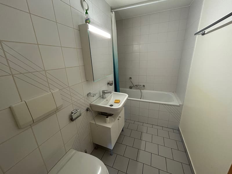 Bathroom with white tiles, white sink, white bathtub, white toilet, white cabinet, mirror with light