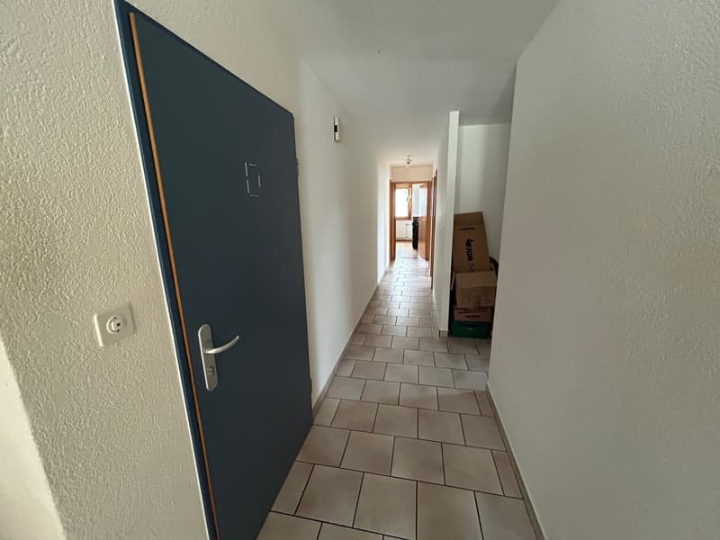 Empty hallway with tiled floor, white walls, and a door leading to another room.