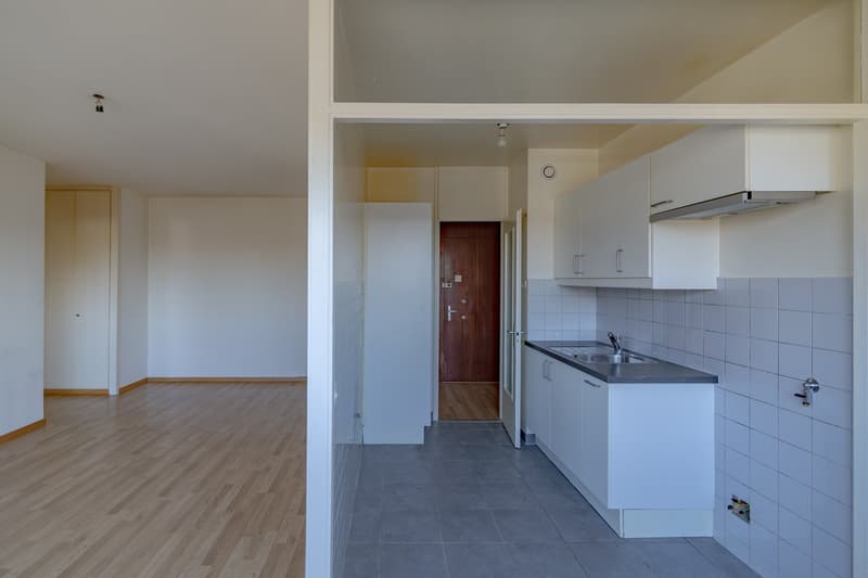 Empty kitchen with white cabinets, wooden floor, white tiles, sink, faucet, and wooden door.