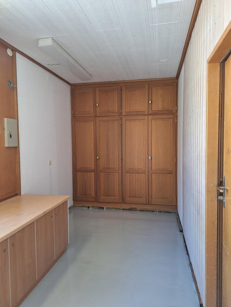 empty room, wooden cabinets, white walls, gray floor, ceiling lights, exit door