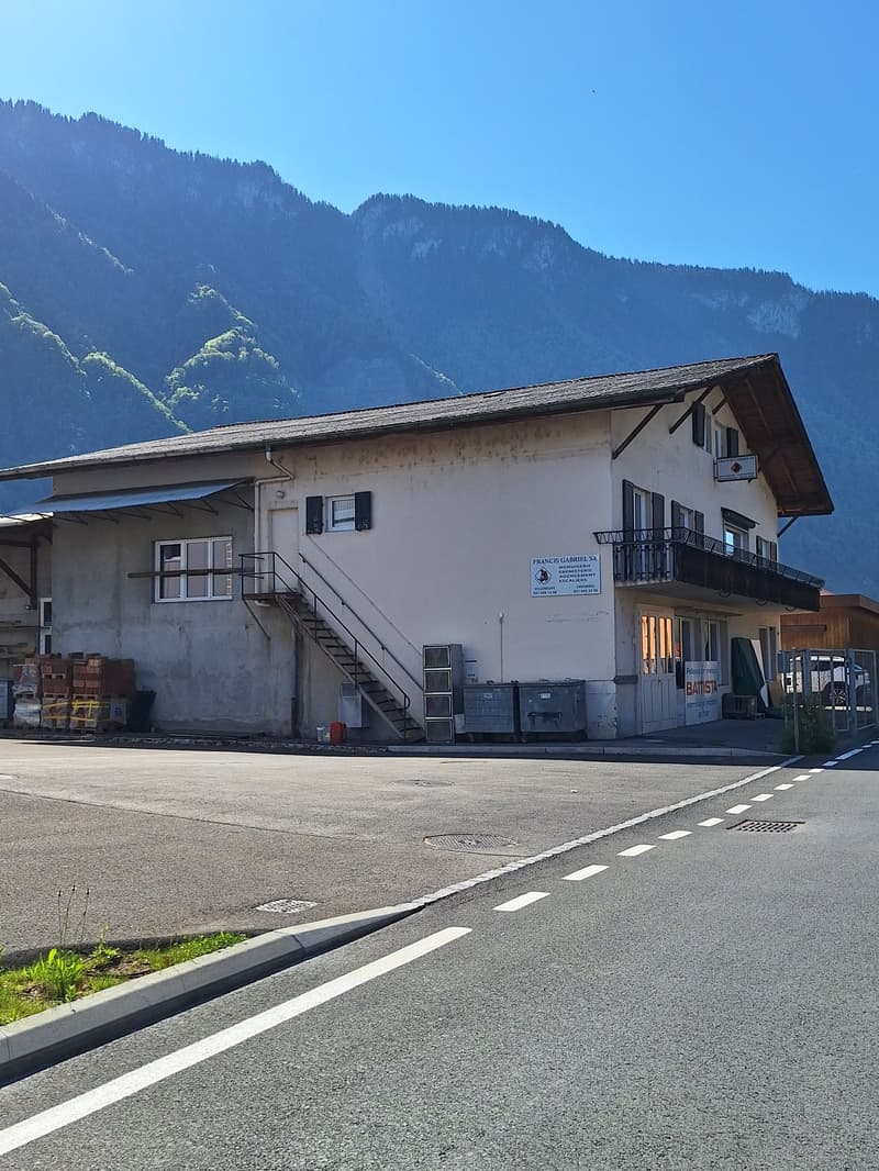 Exterior of a commercial or residential building, white exterior, balconies, stairs, garage-like extension at back, mountain backdrop