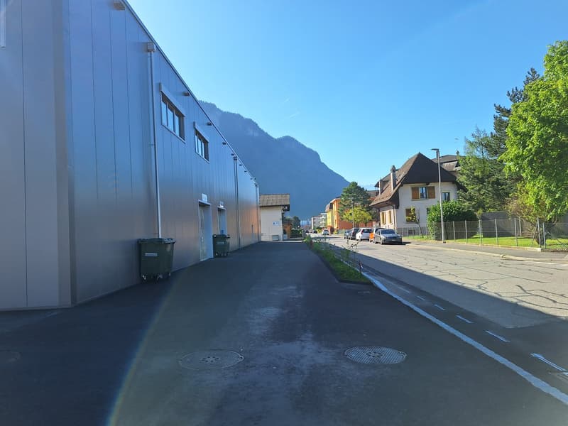 Empty road, large building, mountains in the distance, cars parked on the road