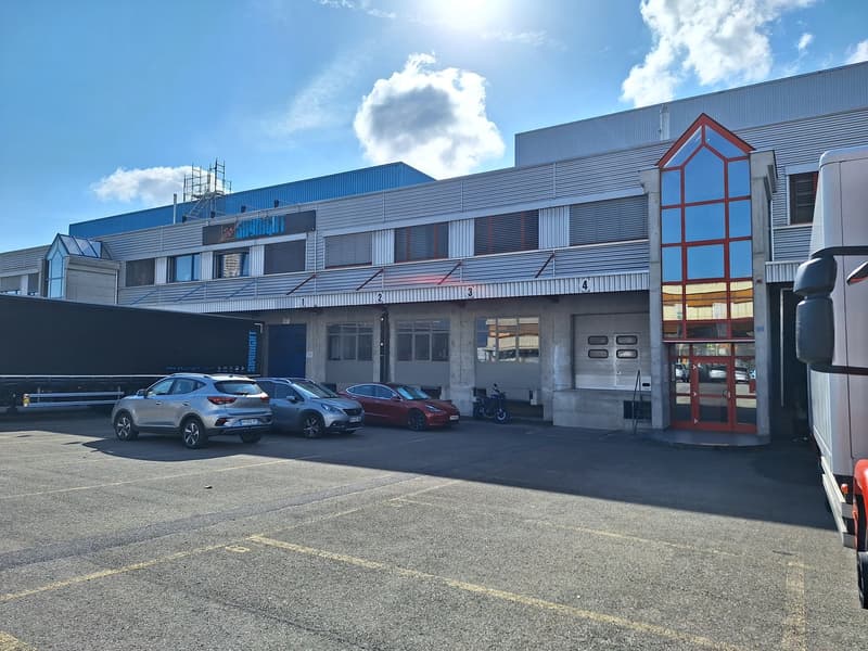 Industrial building with multiple units, large parking area, several cars parked