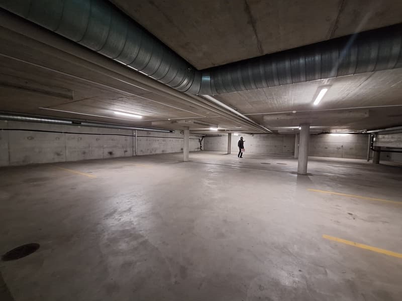 Empty parking lot with concrete floor, yellow markings, and metal beams on the ceiling