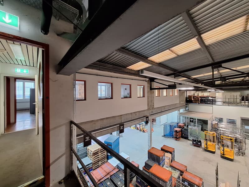 Warehouse with high ceilings, metal beams, multiple windows, storage boxes, forklifts, and a large open space.