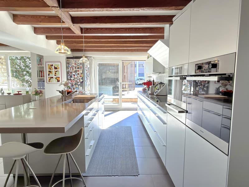 modern white kitchen, gray tile flooring, central island with stools, double oven, refrigerator, large windows, exposed wooden beams