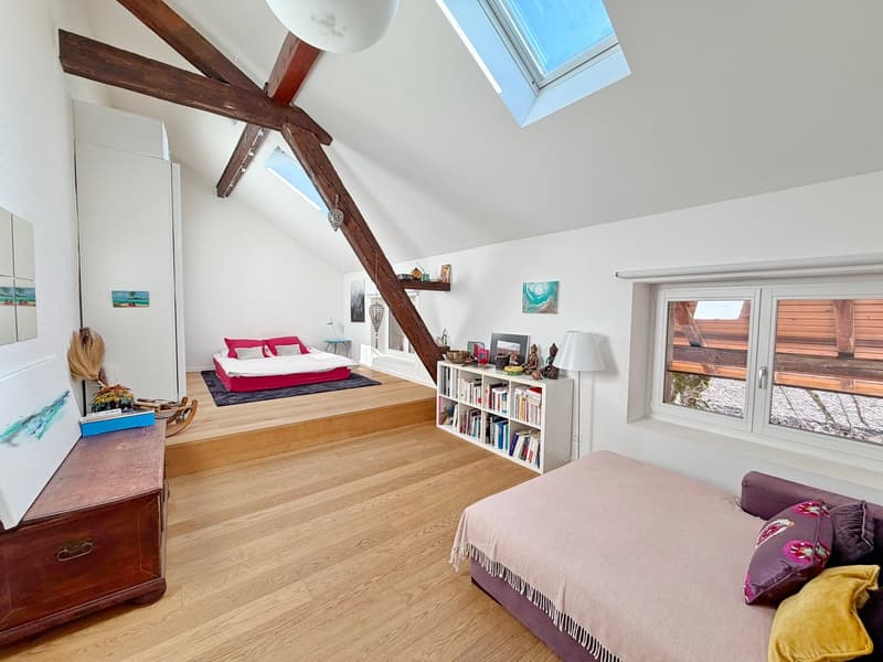 A room with wooden floors, white walls, two beds, a small rug, and a wooden chest of drawers.