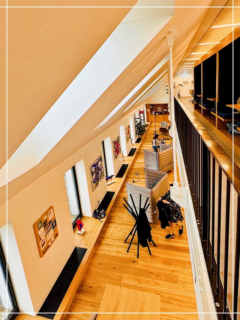 open space with wood floors, windows, benches, wall art, metal railings, balcony, seating area, and black coat rack