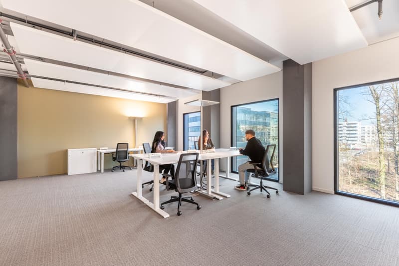 Spacious open-plan office with large windows providing a view, white desks and chairs, and a modern, minimalist design.