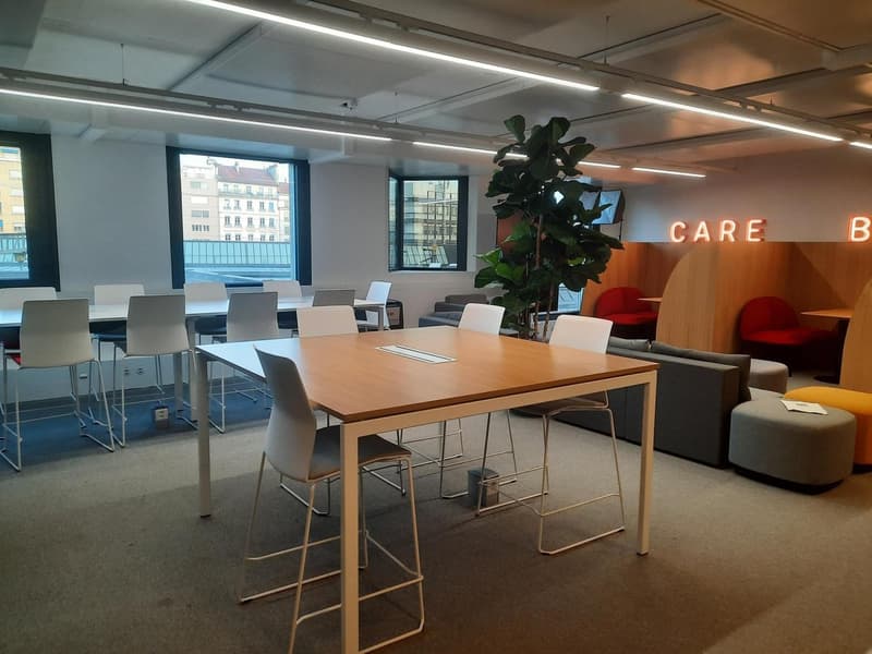 meeting room with rectangular conference table and white chairs, large windows, decorative plant, grey couch, red chairs, ottomans