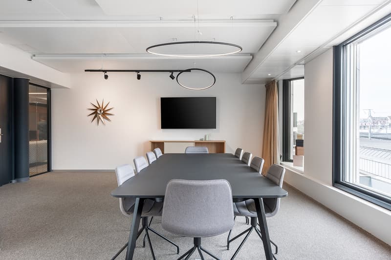 empty conference room, long rectangular table, chairs, wall clock, mounted TV, carpeted floor