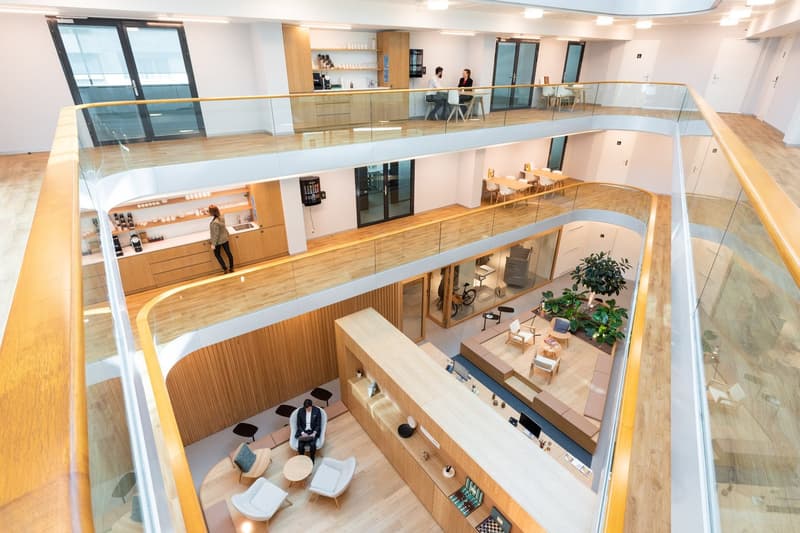 Open-concept office space with multiple levels, glass walls, wooden floors and furniture, kitchenette area, and lounge seating