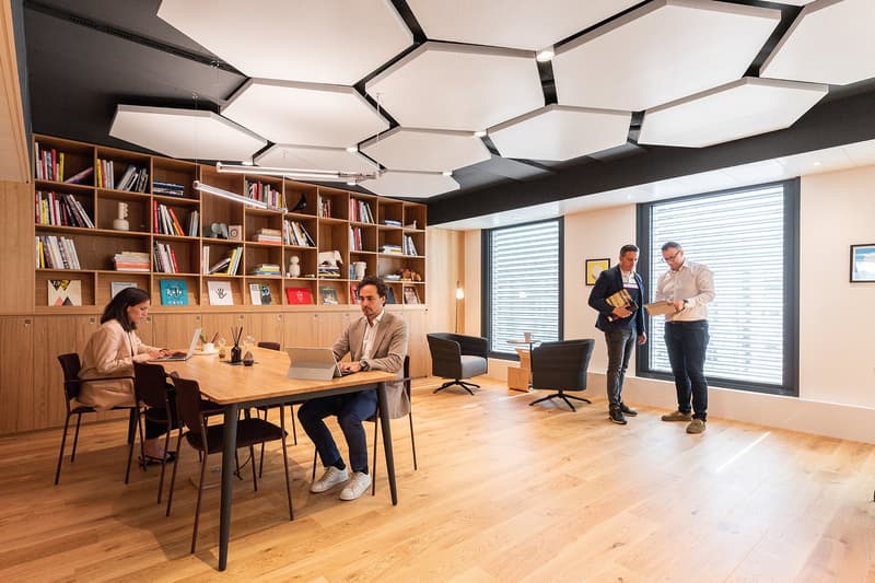 Wooden floors, bookshelves, hexagonal ceiling design, modern furniture, office setup with people working