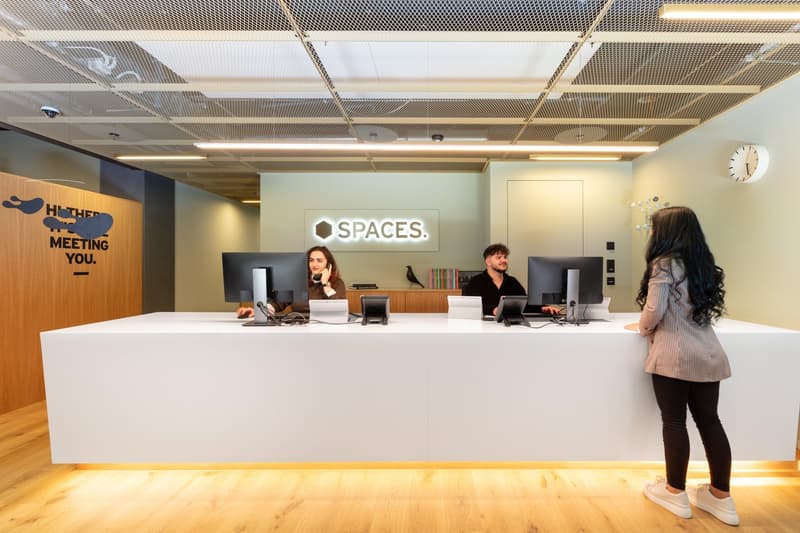 Reception desk, wooden floors, white walls, monitor screens, clock, wooden panel with text, modern office equipment