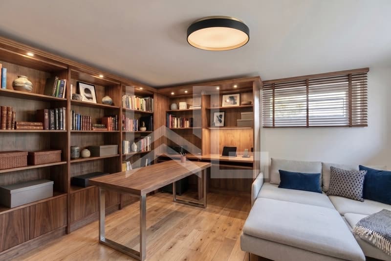 Corsier / a room with a couch, desk, and wooden bookshelves in a home