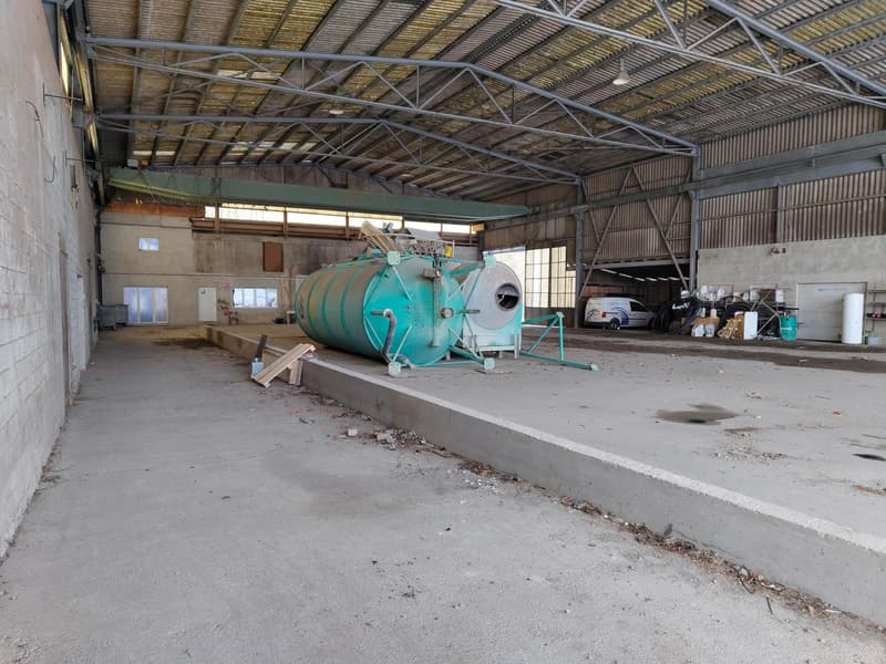 industrial building, metal roof structure, large open space, concrete walls, a green large machine, items and tools scattered around