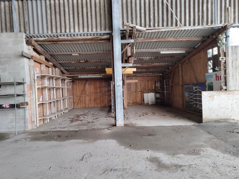 Large empty warehouse, metal structure, wooden walls, concrete floor, storage shelves on the side