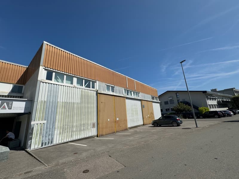 Industrial building with brown and white exterior, large windows, two large doors, cars parked in front