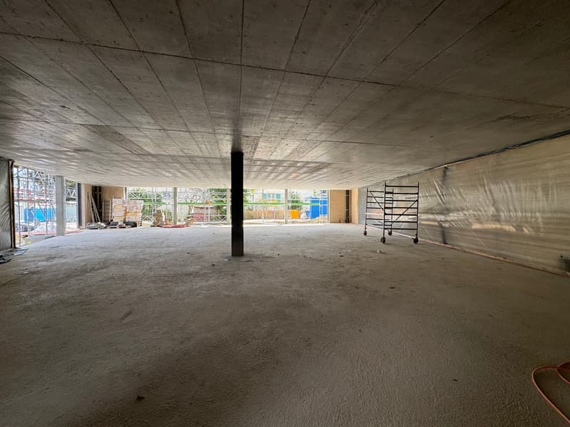 Empty room with concrete floor, walls, and ceiling. Construction materials and equipment visible.