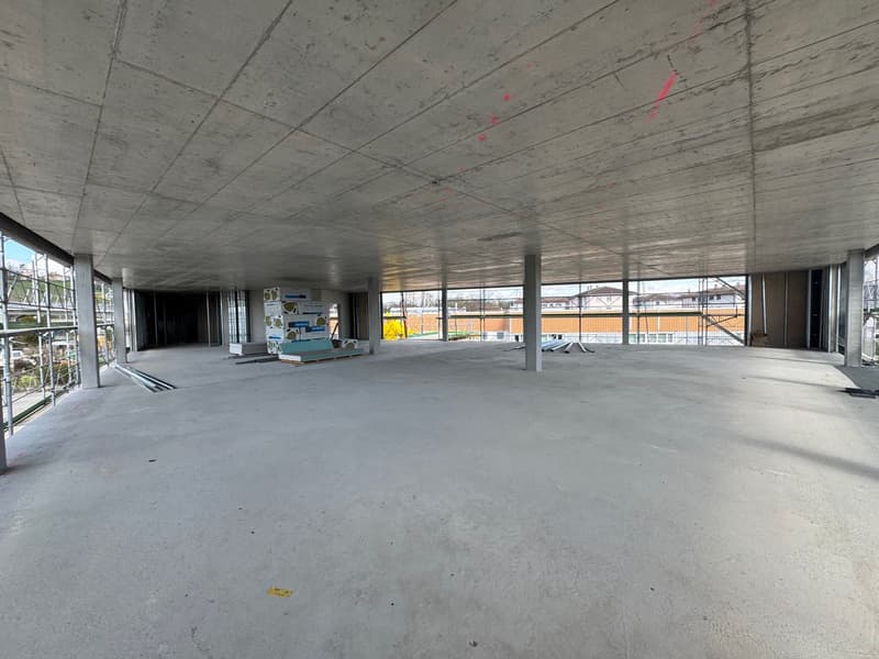 Empty room with concrete floor, high ceiling, large windows, construction materials present