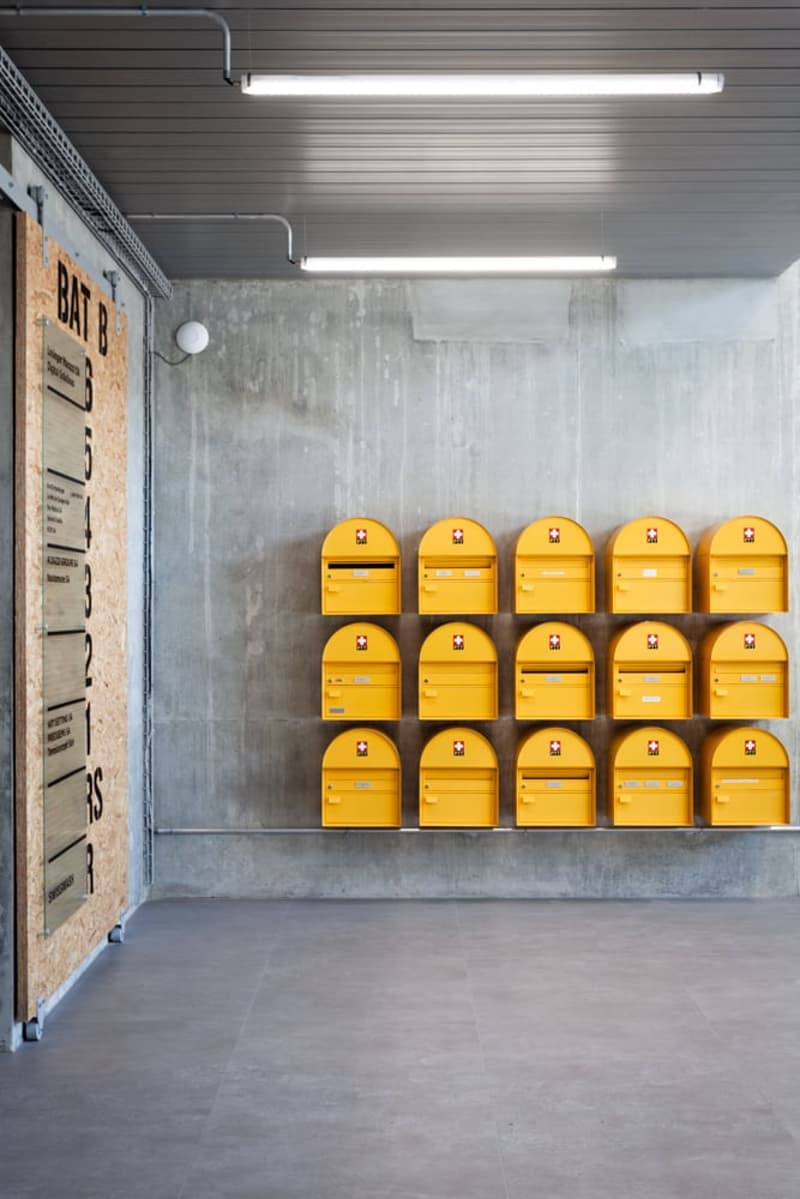 The image shows a storage facility with rows of yellow lockers or mailboxes on the wall. The space has a concrete floor and gray walls with fluorescent lighting fixtures overhead.