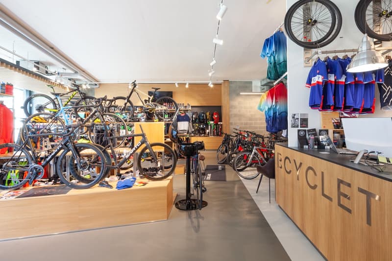 The image shows the interior of a bicycle shop. There are various bicycles, both road bikes and mountain bikes, displayed on the walls and floor. The shop also has a counter with the word 'Cyclist' written on it, indicating it is a bicycle shop. There are