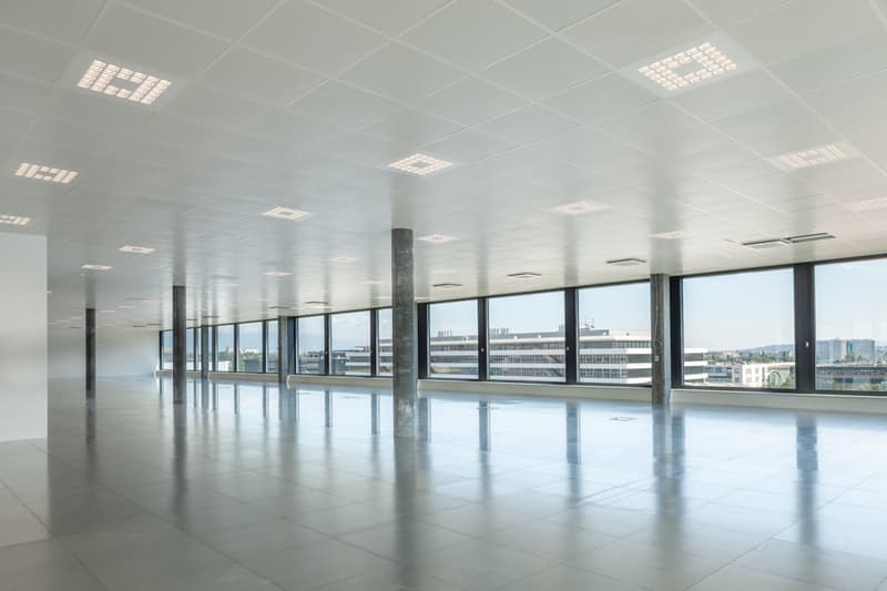 Large open office space with floor-to-ceiling windows offering a view of the city skyline, polished concrete floors, and recessed lighting in the ceiling.