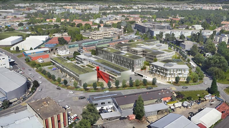 Aerial view of a city with a mix of residential and commercial buildings, including multi-story office buildings, a large sports arena or event center, and various other structures. The city appears to be surrounded by green spaces and trees. There are vi