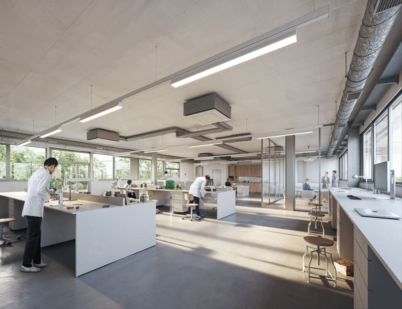 Open concept office space with modern design, including large windows, exposed ceiling, and various workstations and seating areas. The space features a kitchen area with a dishwasher visible.
