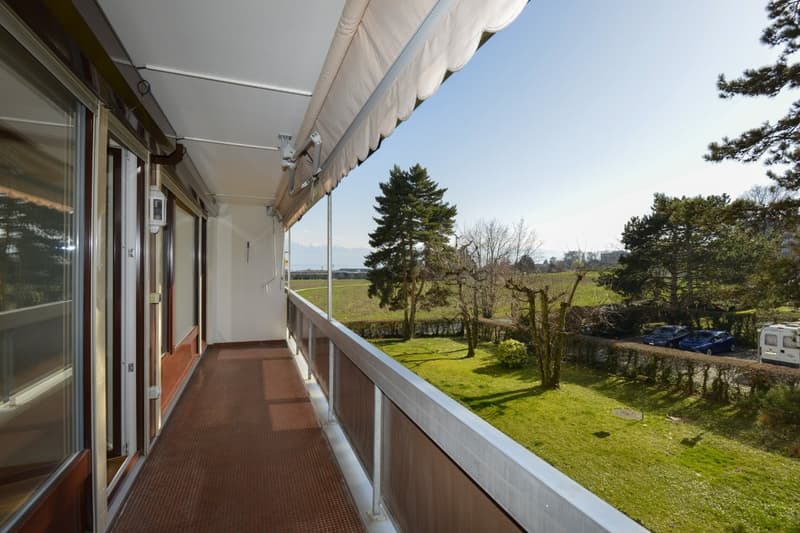 Balcony with a railing, outdoor furniture, awning, green lawn, tree, car