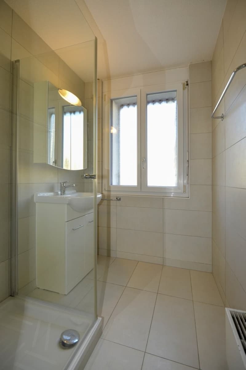 Tiled floor, glass shower enclosure, white cabinet, sink, window, tiled walls, radiator