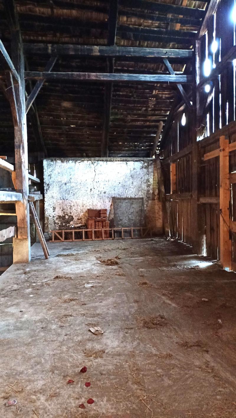 Old, wooden barn with a dirt floor, stacked wooden crates, and a stone wall visible in the background.