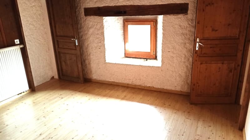 This image shows a rustic room with wooden beams, a wooden window frame, and a wooden floor. The walls appear to be made of plaster or stucco. The room has a simple, minimalist design with a clean and natural aesthetic.
