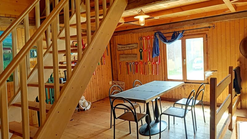Dining area with wooden walls, wooden floor, table and chairs, wooden staircase, light fixture