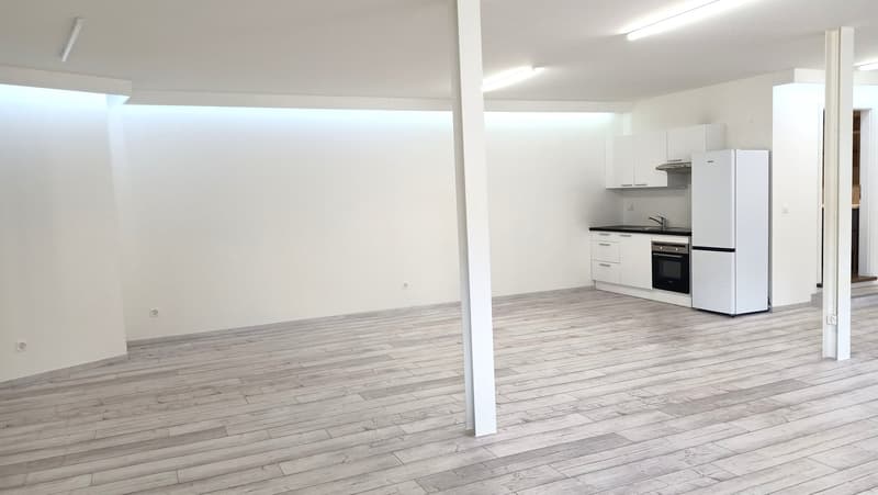 Empty room with a modern design. White walls and floors, central pillar, equipped kitchen in corner.