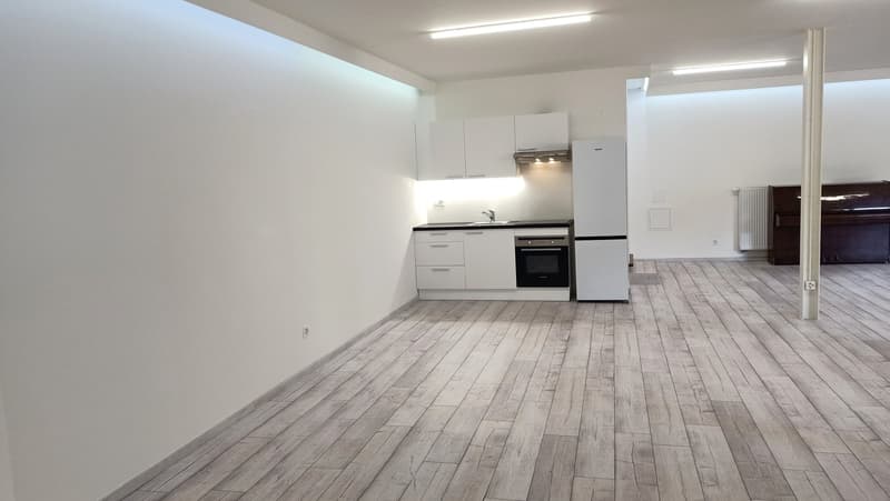 Empty room with wooden floor, white walls, kitchen with sink, gas stove, dishwasher, oven, refrigerator, cabinets