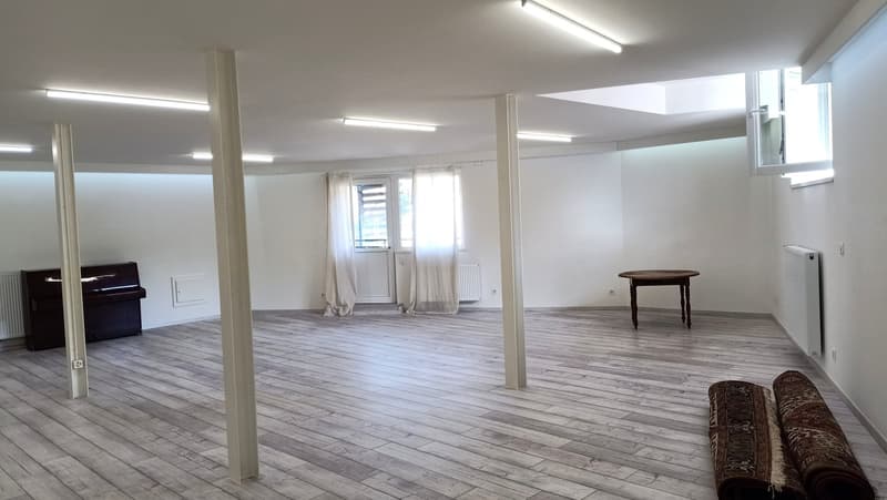 an empty room with wooden flooring, piano, radiator, curtains, windows, small table, beams