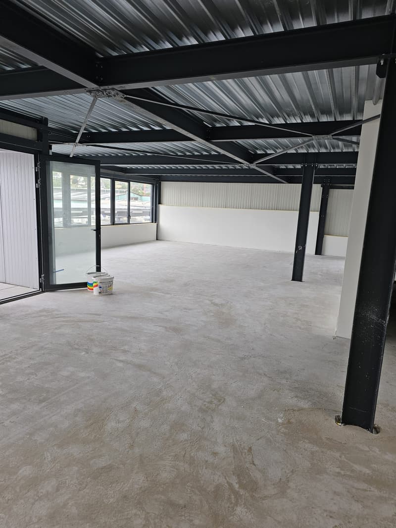 Empty room with concrete floor, metal ceiling, glass doors, and windows, two white buckets with paint