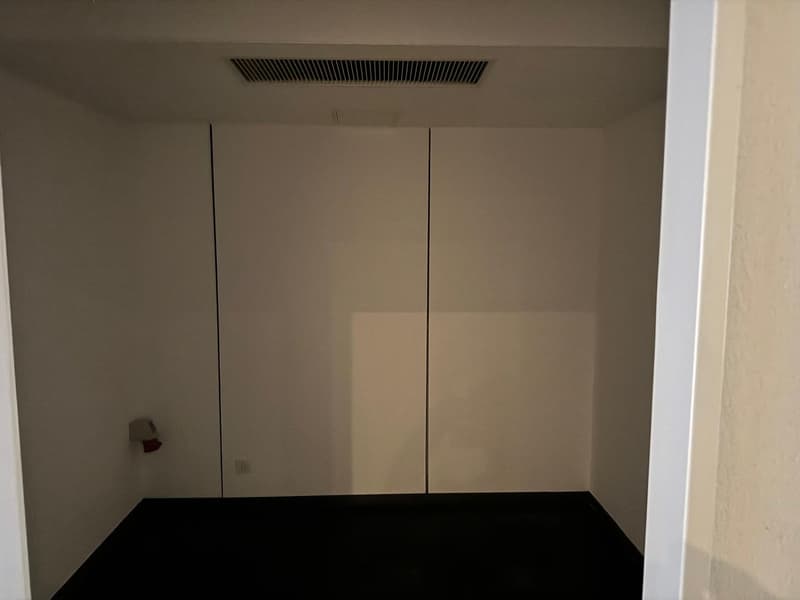 empty room with white walls, black floor, two doors, electrical outlet, vent on ceiling
