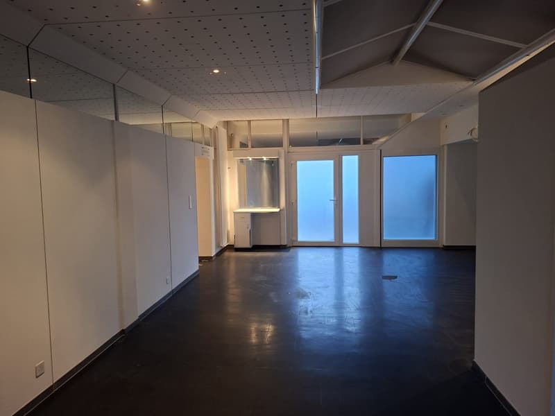 Empty room with white walls, black flooring, large glass doors, small window, small counter.