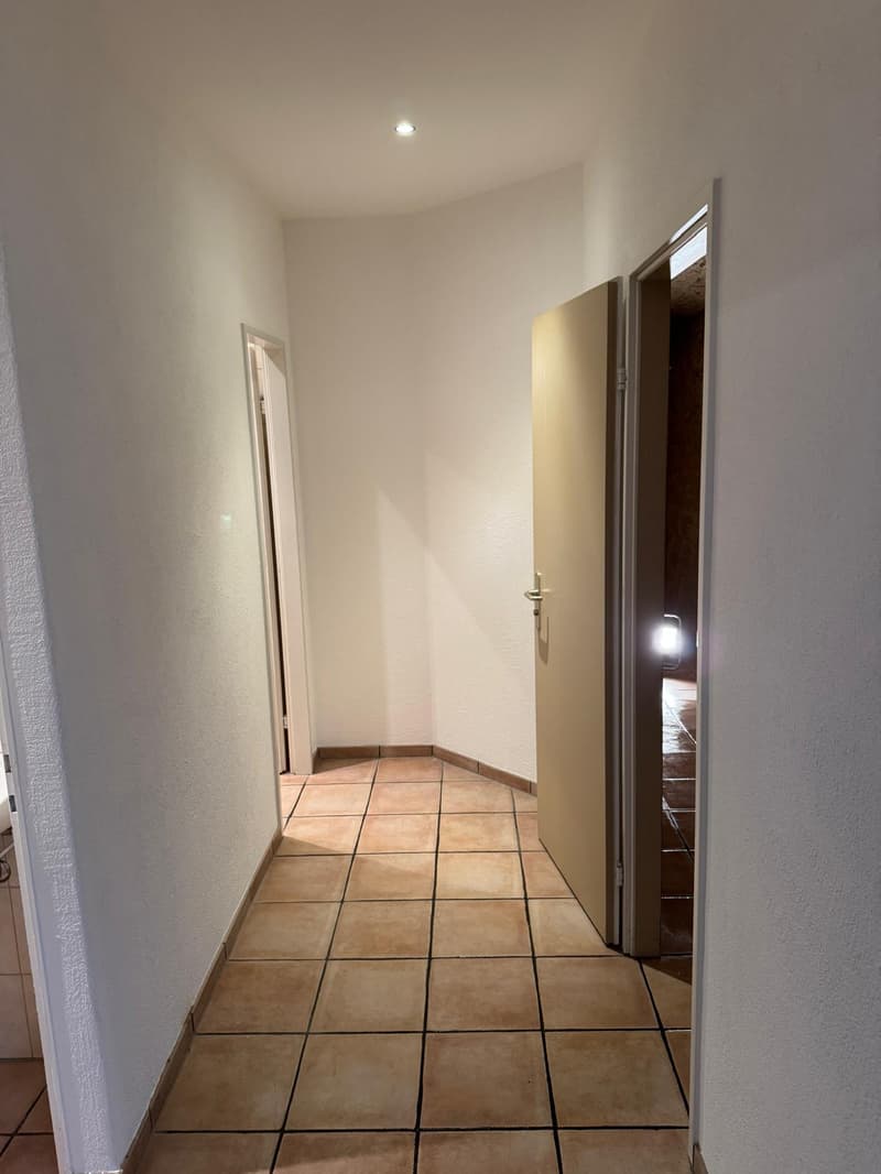 Empty hallway with white walls, tiled floor, open doors, hallway lighting