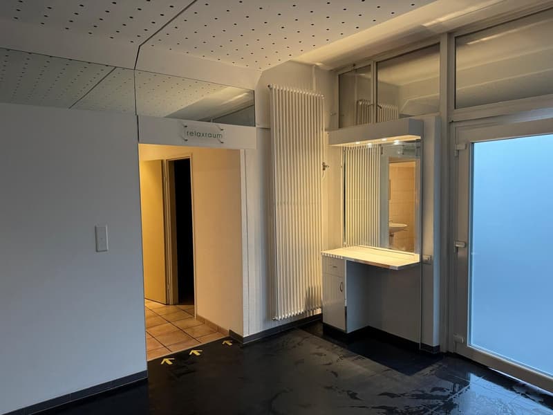 Empty room with a relax room sign, a large mirror and sink, a radiator and a sliding door.