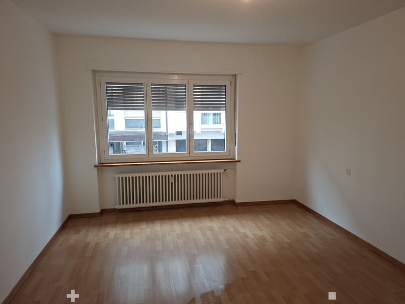 empty room with a window, white walls, wooden floor, radiator