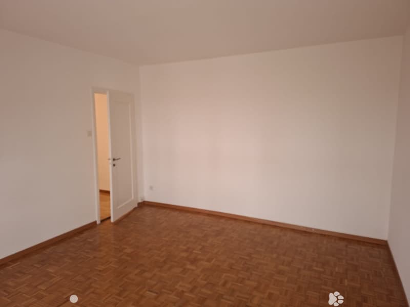 empty room with white walls, wooden parquet flooring, open door leading to another room
