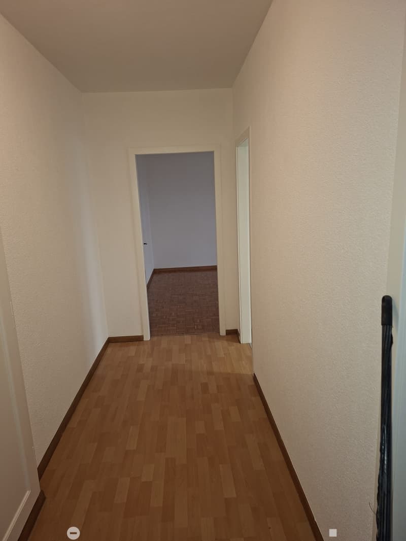 Empty hallway with wooden floor and two doors, one of which leads to a room with wooden parquet floor