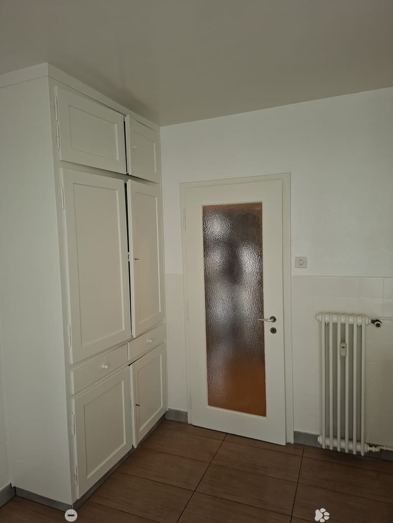 Empty room with wooden floor, a door with glass pane, and a white cupboard with drawers