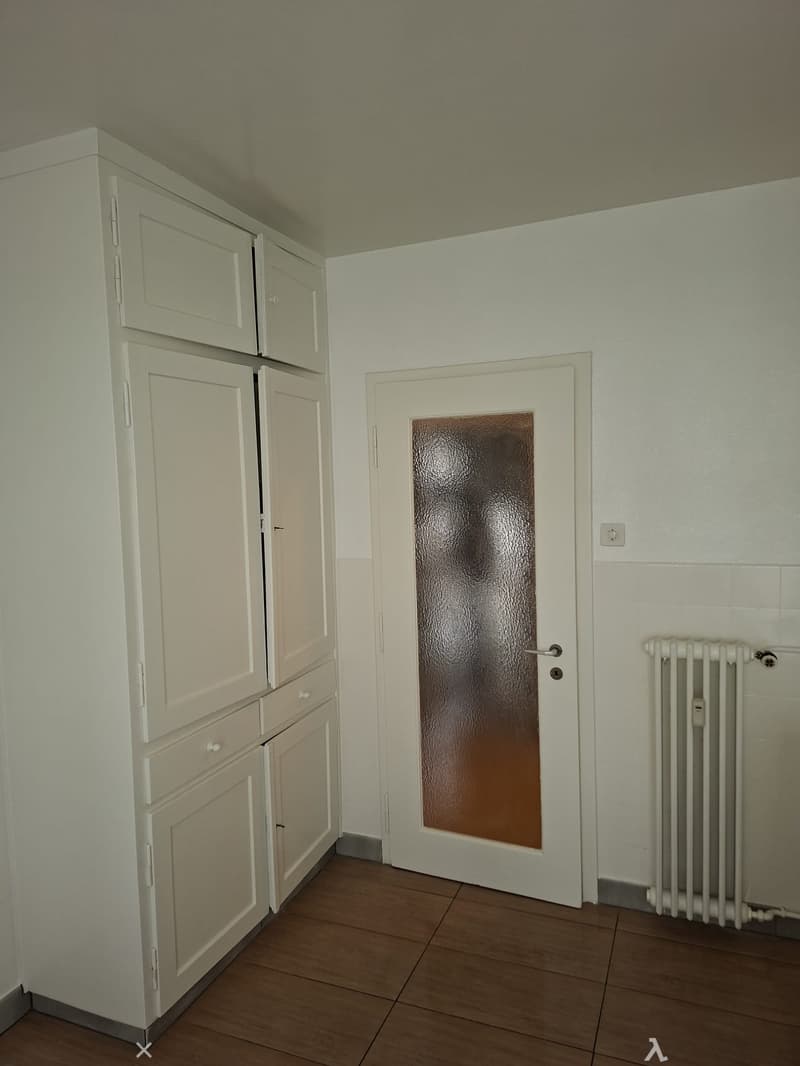 Empty room with wooden floor, a door with glass pane, and a white cupboard with drawers