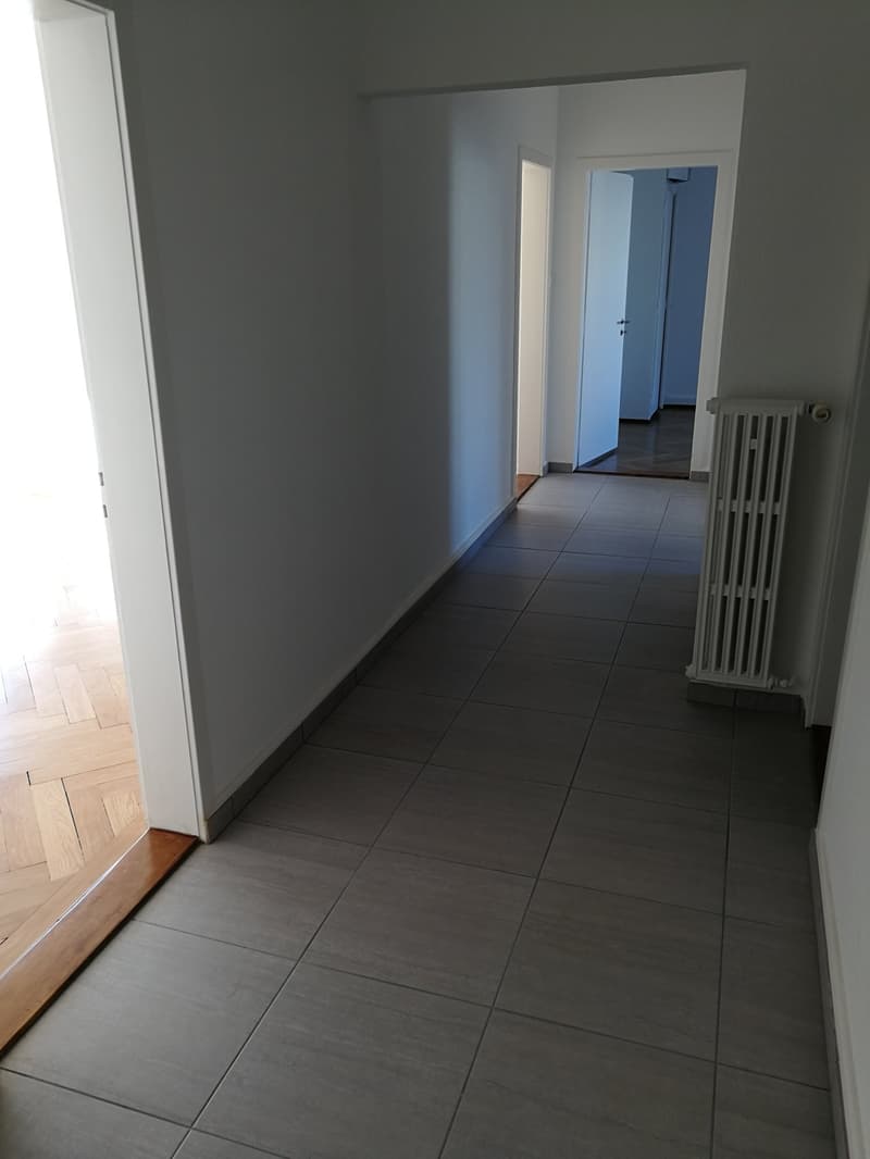 long hallway with white walls, wooden floor, radiator, two closed doors