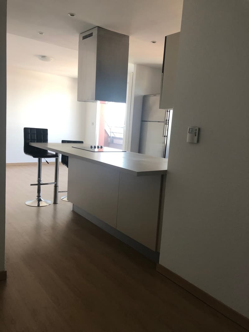 Open kitchen with black chairs, white countertops, gray flooring, and appliances.